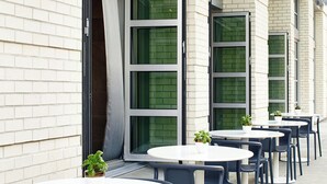 A row of outdoor tables and chairs with potted plants, set against a building with large windows and a brick facade. - AC Hotel by Marriott Portland Downtown, OR (Portland)