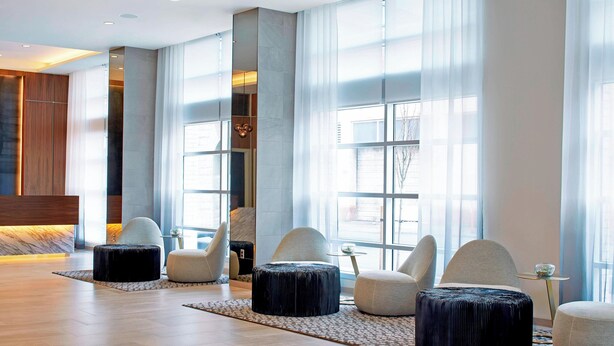 A modern lobby with large windows, a marble reception desk, and several seating areas with ottomans. - AC Hotel by Marriott Portland Downtown, OR (Portland)