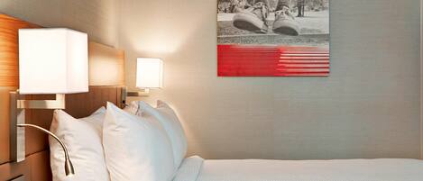 Une chambre d’hôtel avec un lit soigneusement fait, deux lampes de chevet et un tableau encadré au mur.