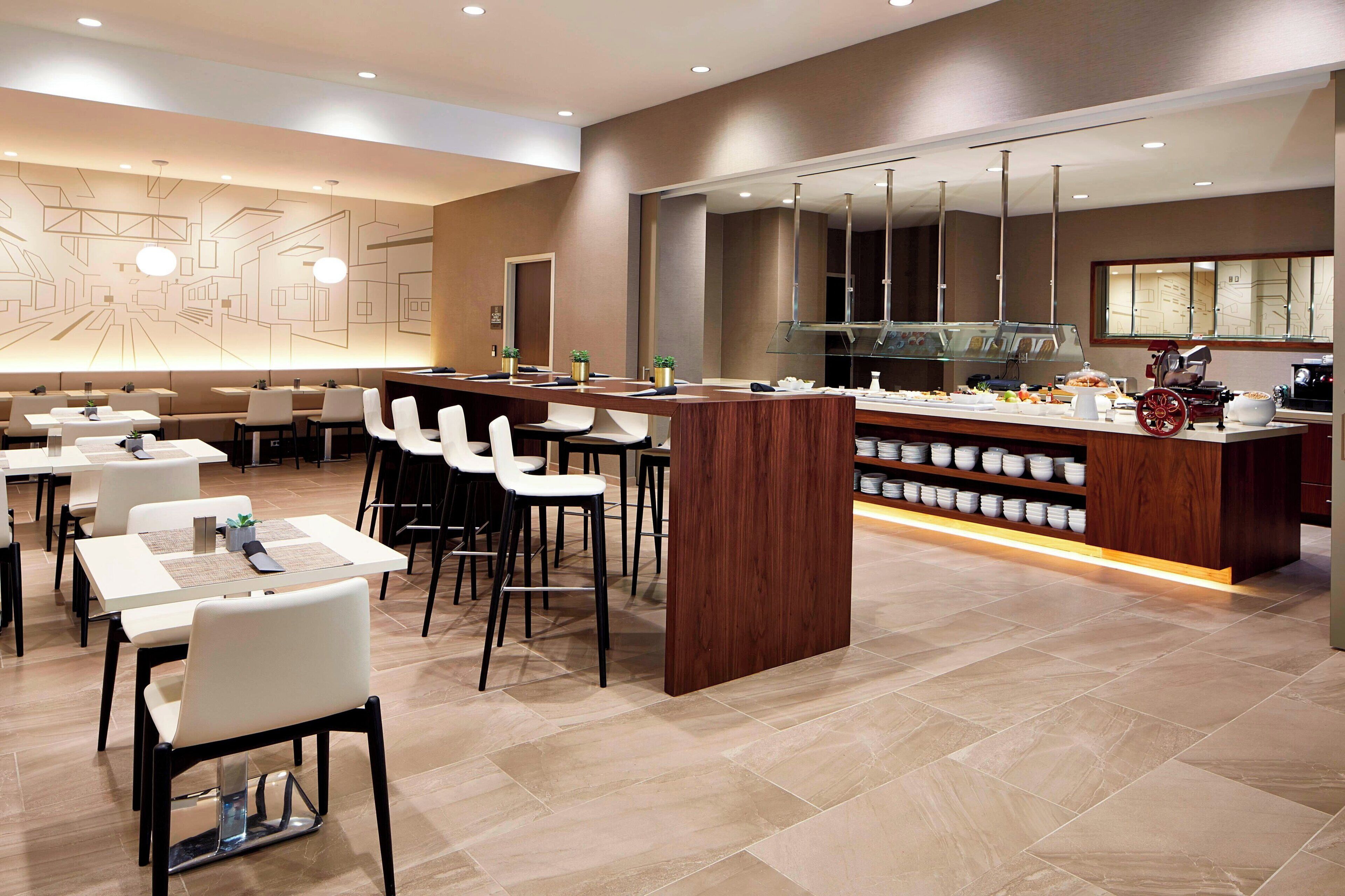 A modern restaurant with a long counter, bar stools, and a variety of seating options including tables and chairs.