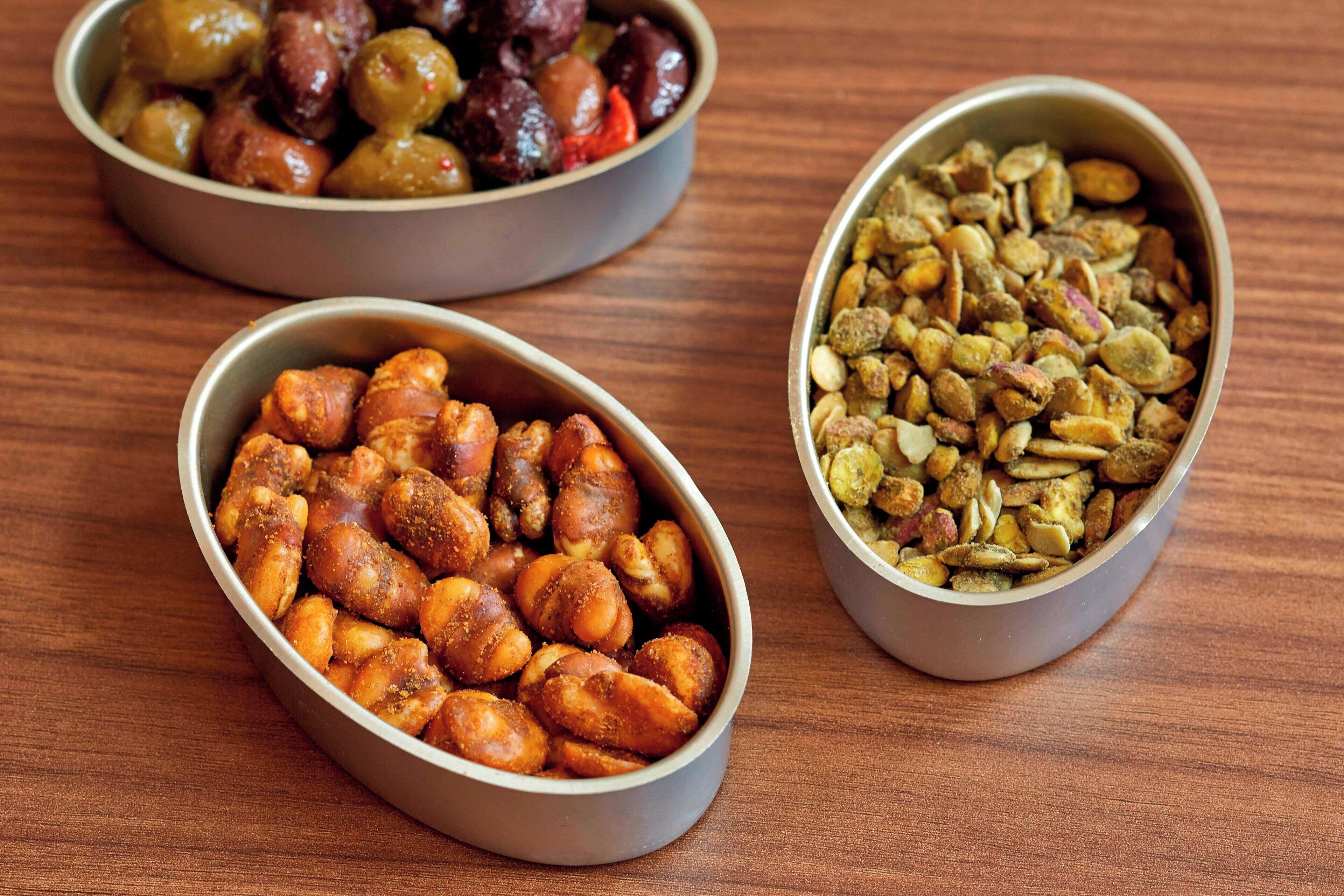 Three bowls of nuts on a wooden table.