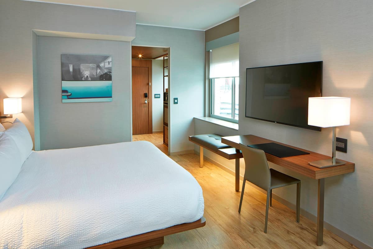 A hotel room with a large bed, a desk with a chair, a TV, and a window.