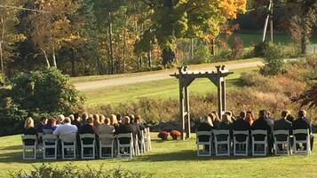 Ceremonia de boda al aire libre con invitados sentados en filas frente a un arco de madera.