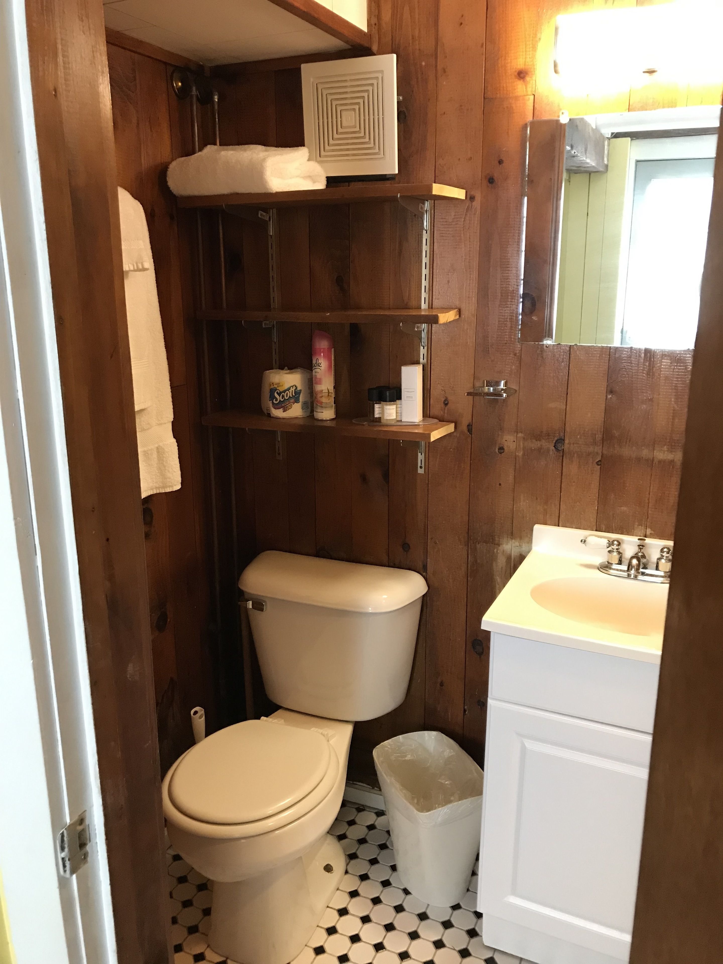 Een kleine badkamer met toilet, een wastafel en een plank met toiletartikelen.
