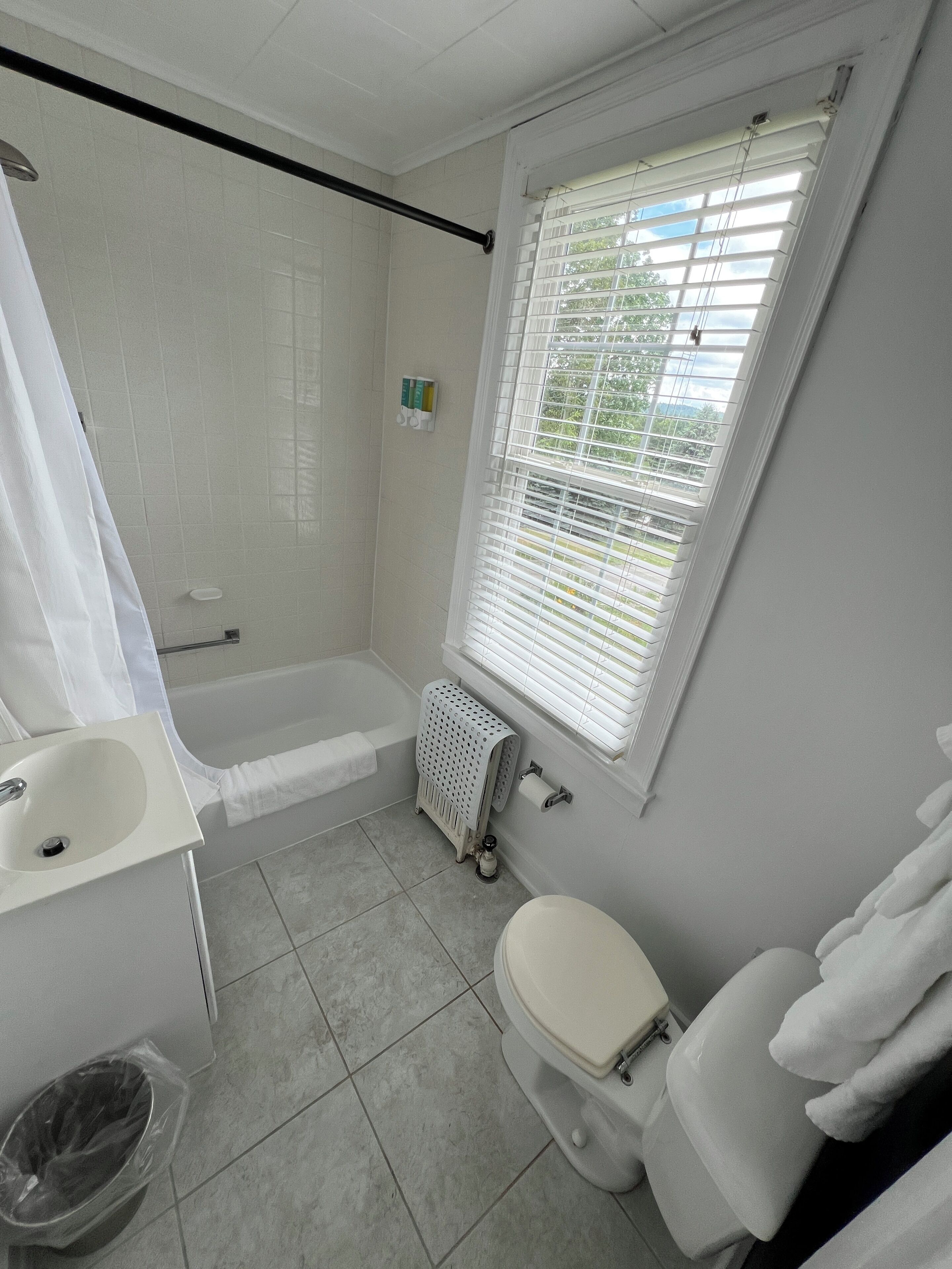 A bathroom with a bathtub, toilet, sink, and a window with blinds.