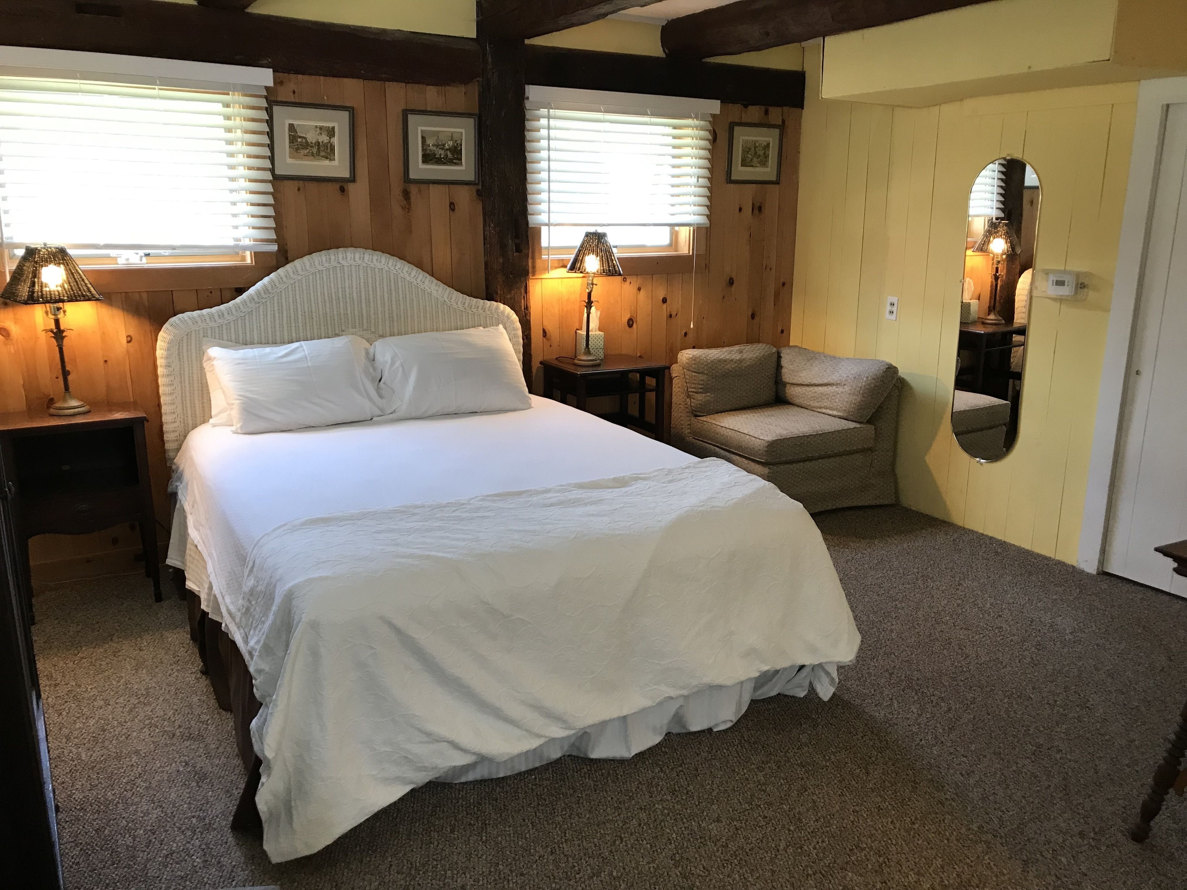 A bedroom with a large bed, two bedside tables, a chair, and a mirror.