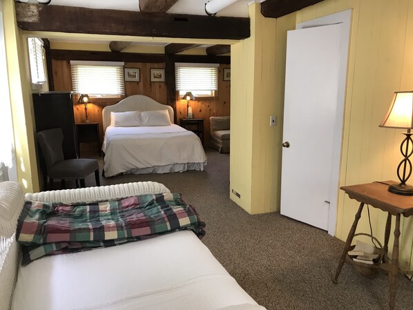 Una habitación acogedora con una cama, una silla, una mesita con una lámpara y una puerta.