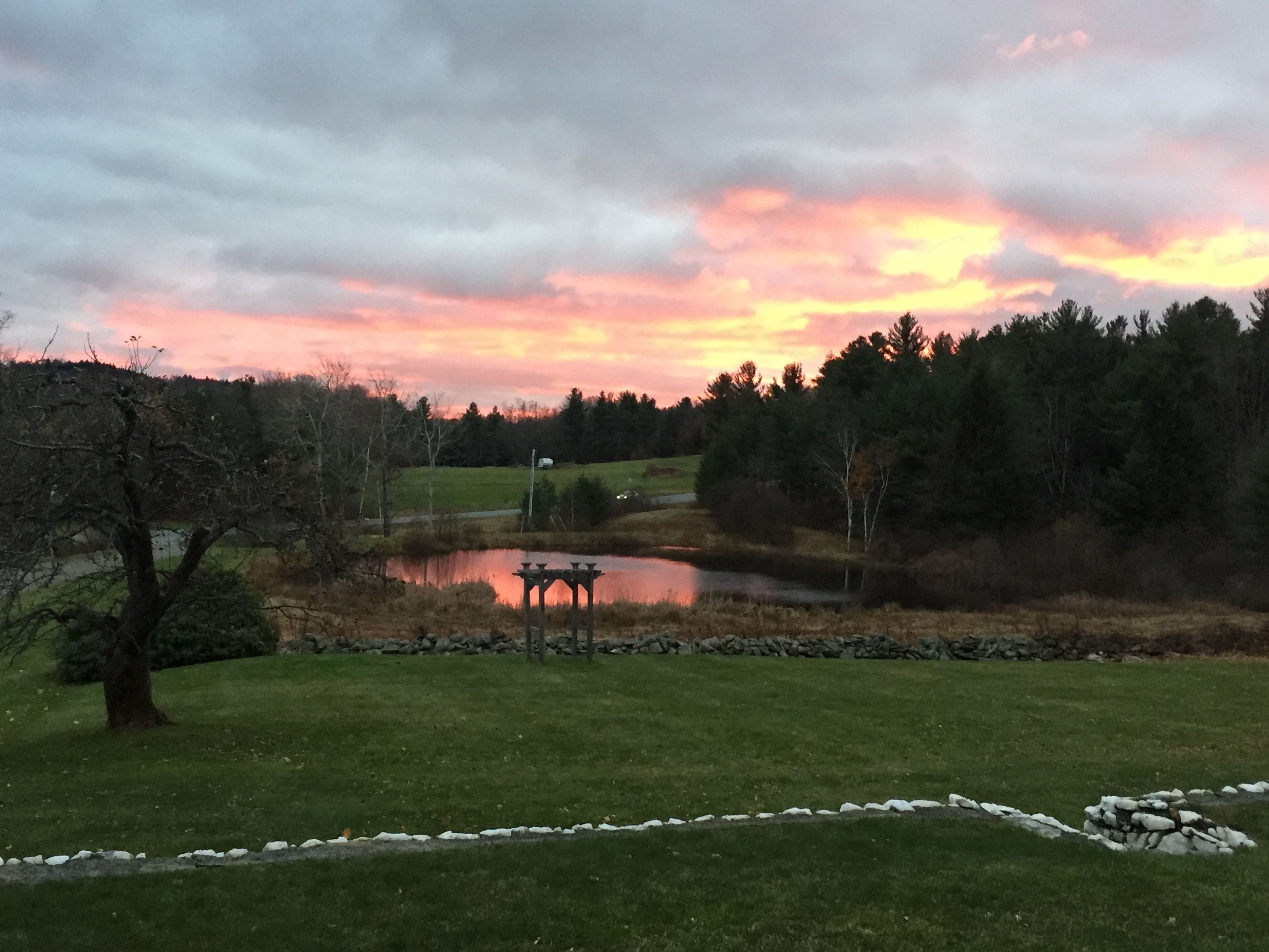 A serene landscape with a pond, a gazebo, and a stone wall.