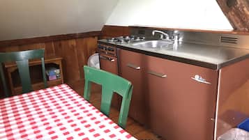 A compact kitchen with a red and white checkered tablecloth, a green chair, and a small fan.