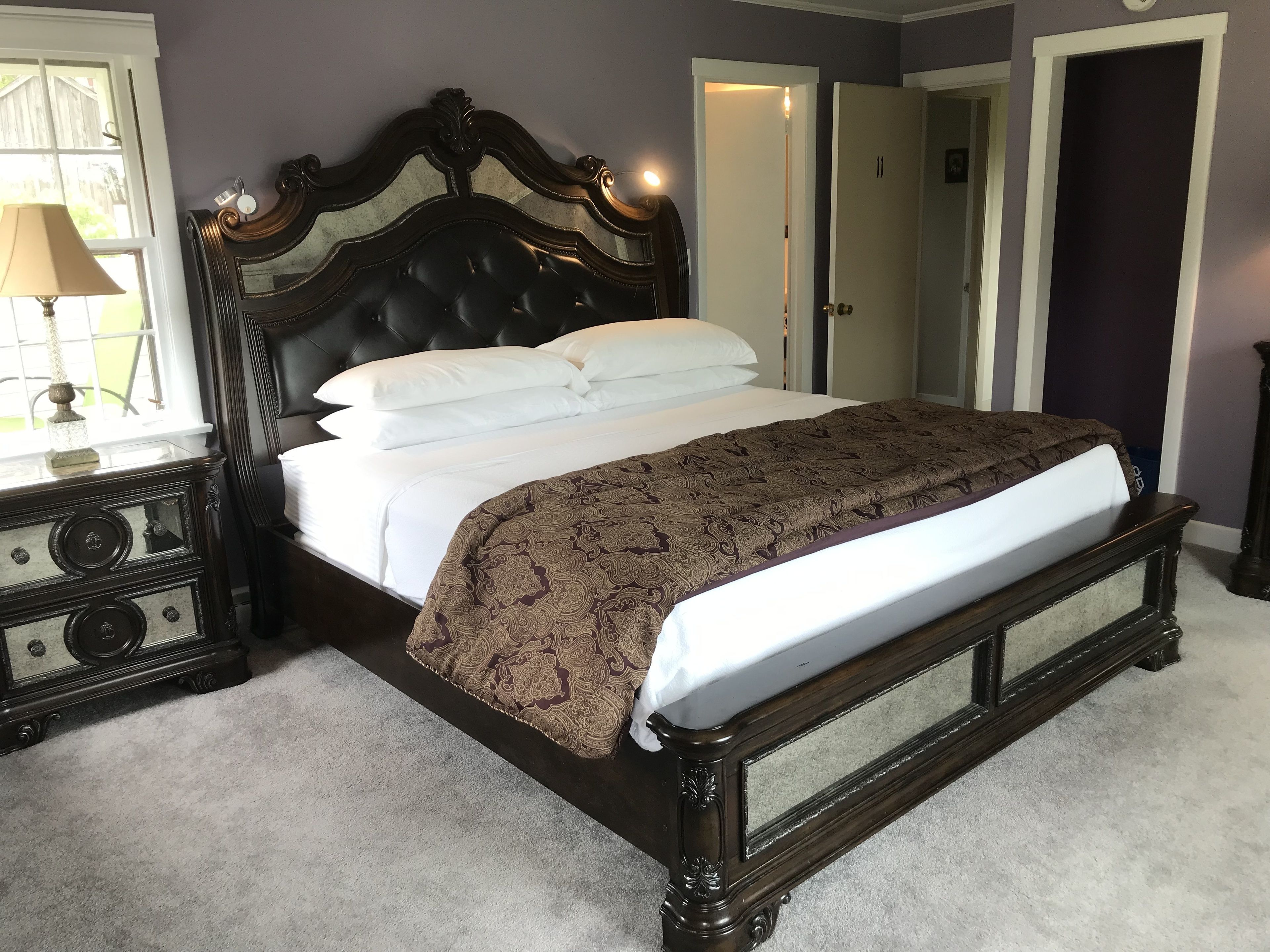 Une chambre à coucher avec un grand lit, une table de chevet, une lampe et une porte.