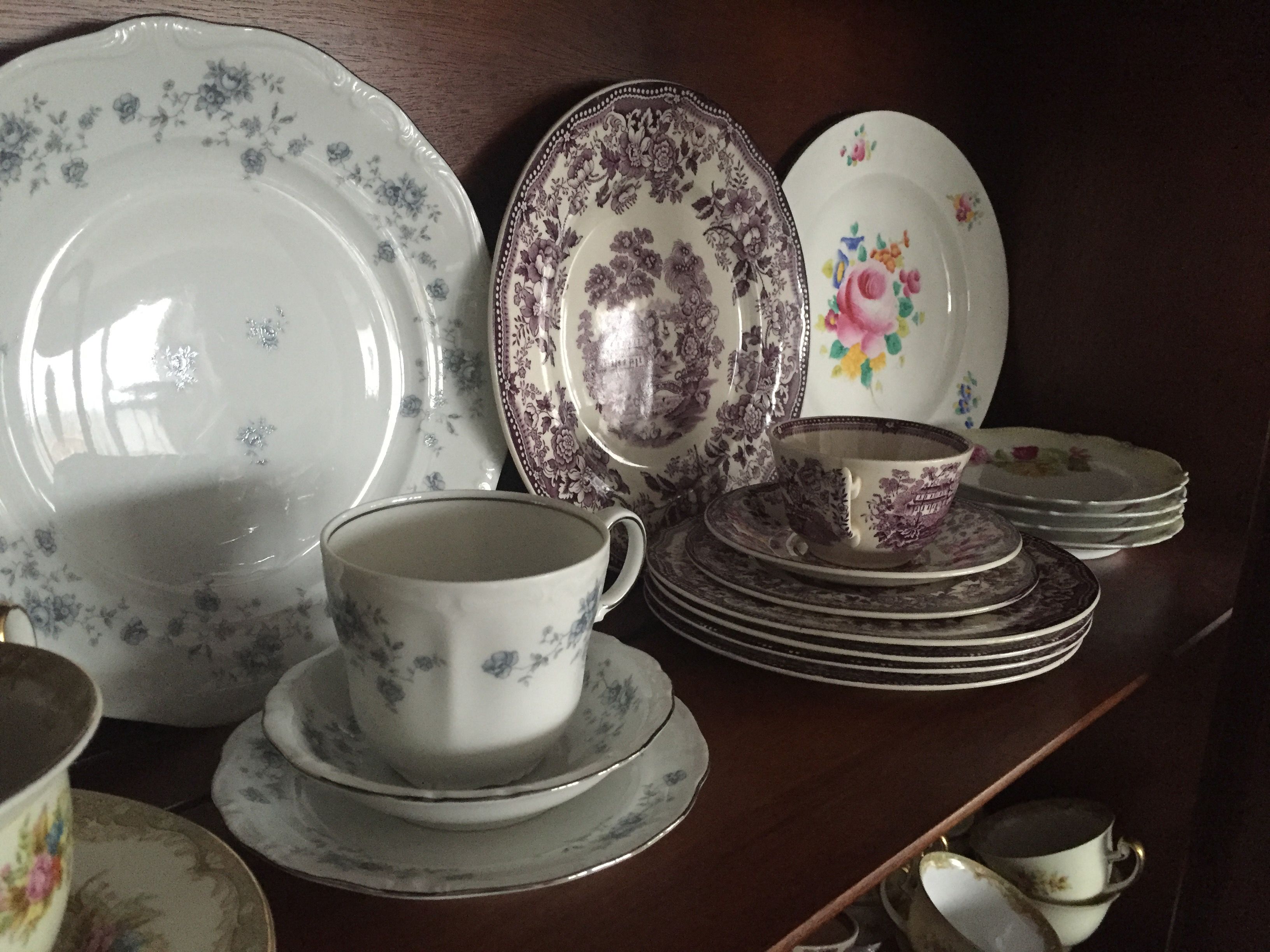A collection of white and patterned ceramic dishes and cups on a wooden shelf.