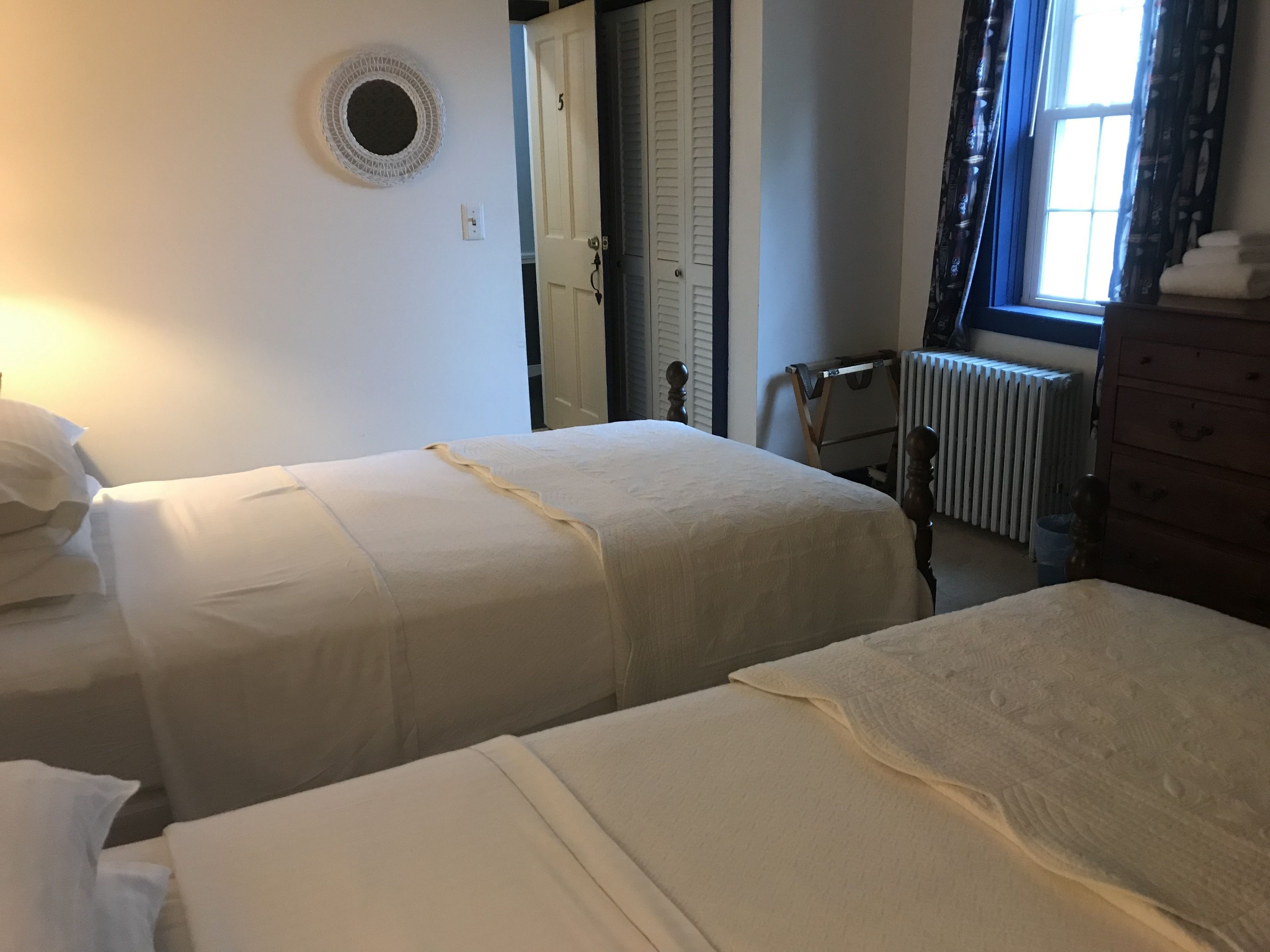 Een slaapkamer met twee enkele bedden, een radiator, een raam met gordijnen, een deur en een rond inbouwlamp.