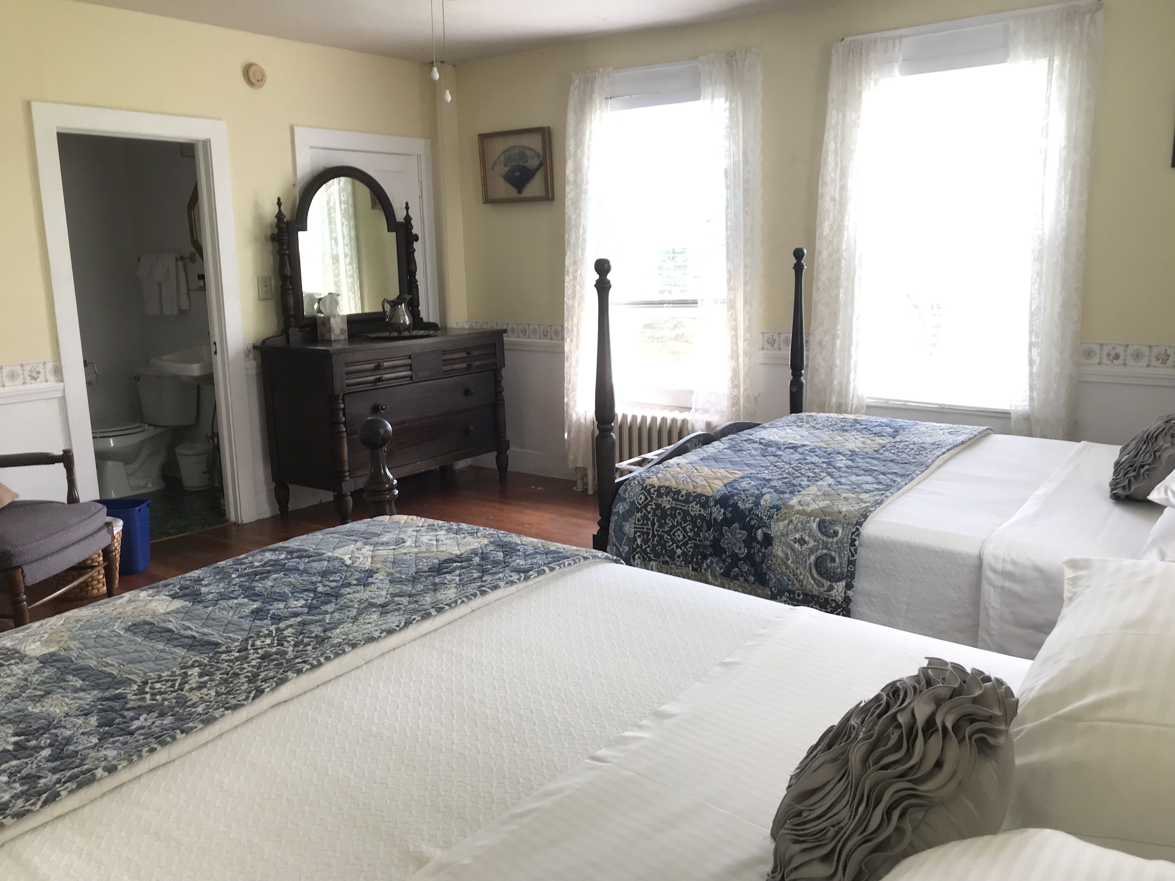 A bedroom with two beds, a dresser, a mirror, and a window with curtains.