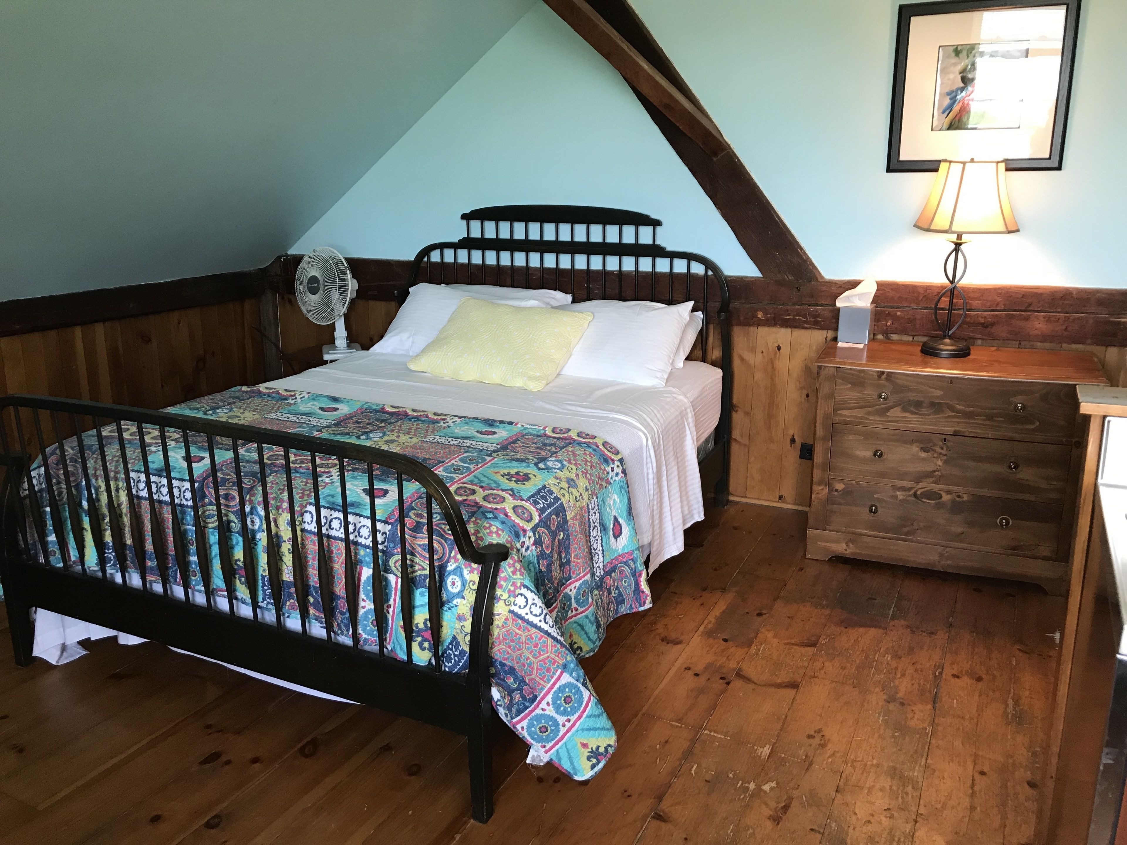 A bedroom with a wooden bed, a nightstand, a lamp, and a ceiling fan.