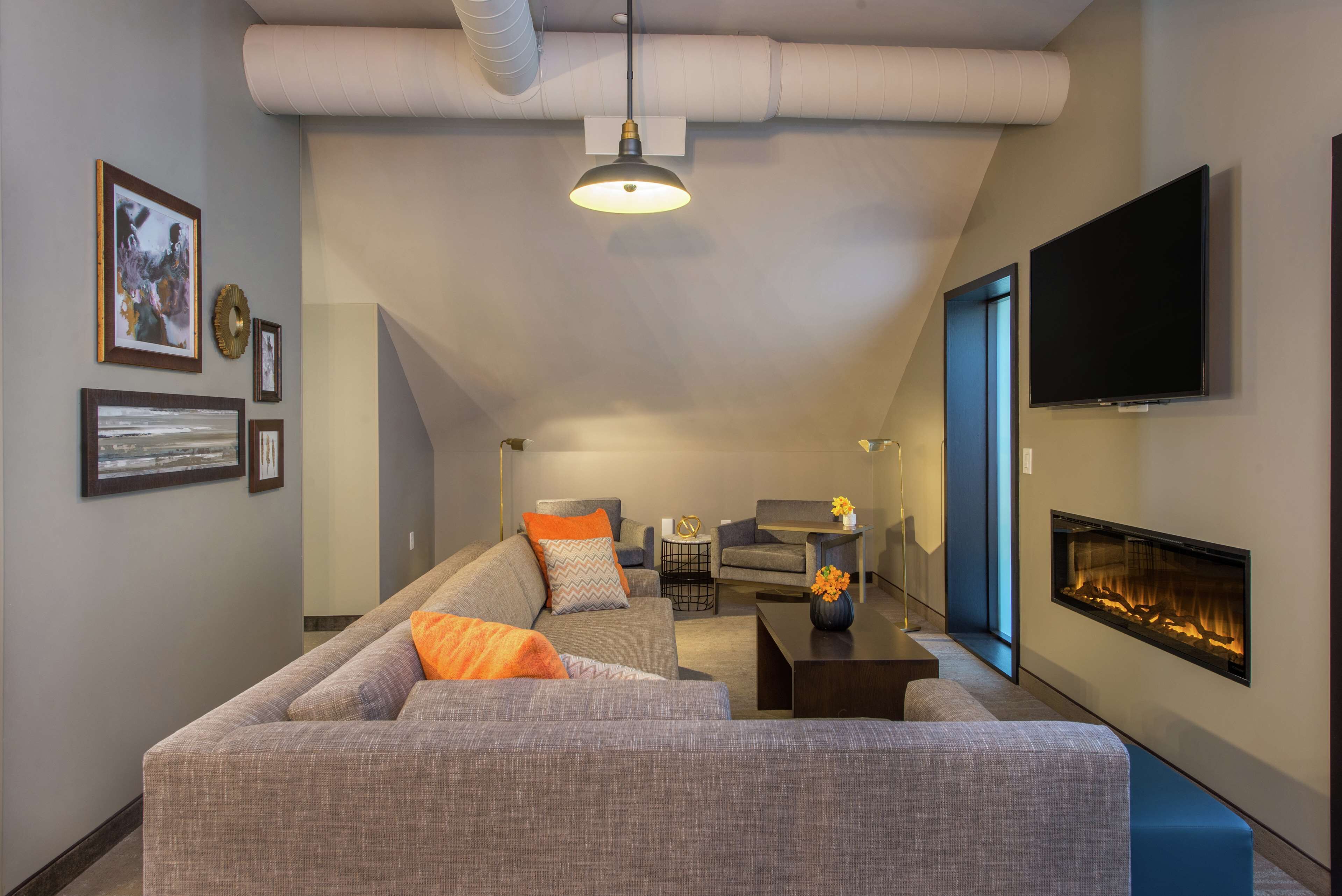 A modern living room with a sectional sofa, a flat-screen TV, a fireplace, and a ceiling with exposed ductwork.