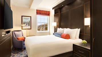 Une chambre d’hôtel avec un grand lit, une chaise, une télévision, une fenêtre donnant sur un beau paysage et un tableau encadré au mur.