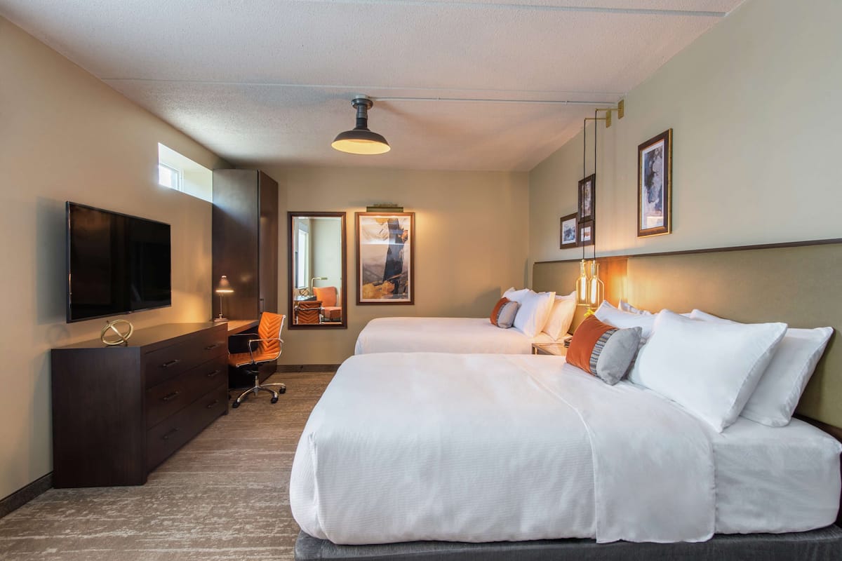 A hotel room with two beds, a TV, a desk, and a chair.