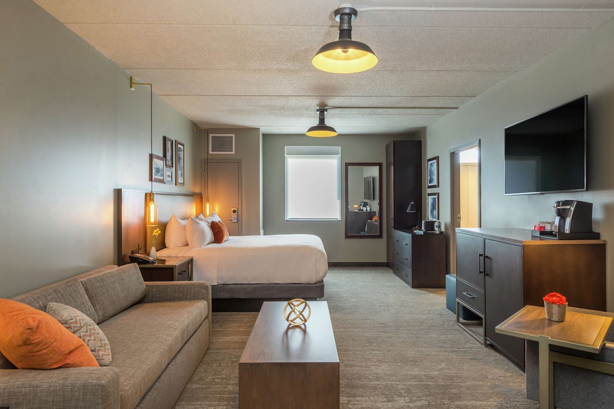 A hotel room with a bed, sofa, coffee table, TV, and a desk with a chair.