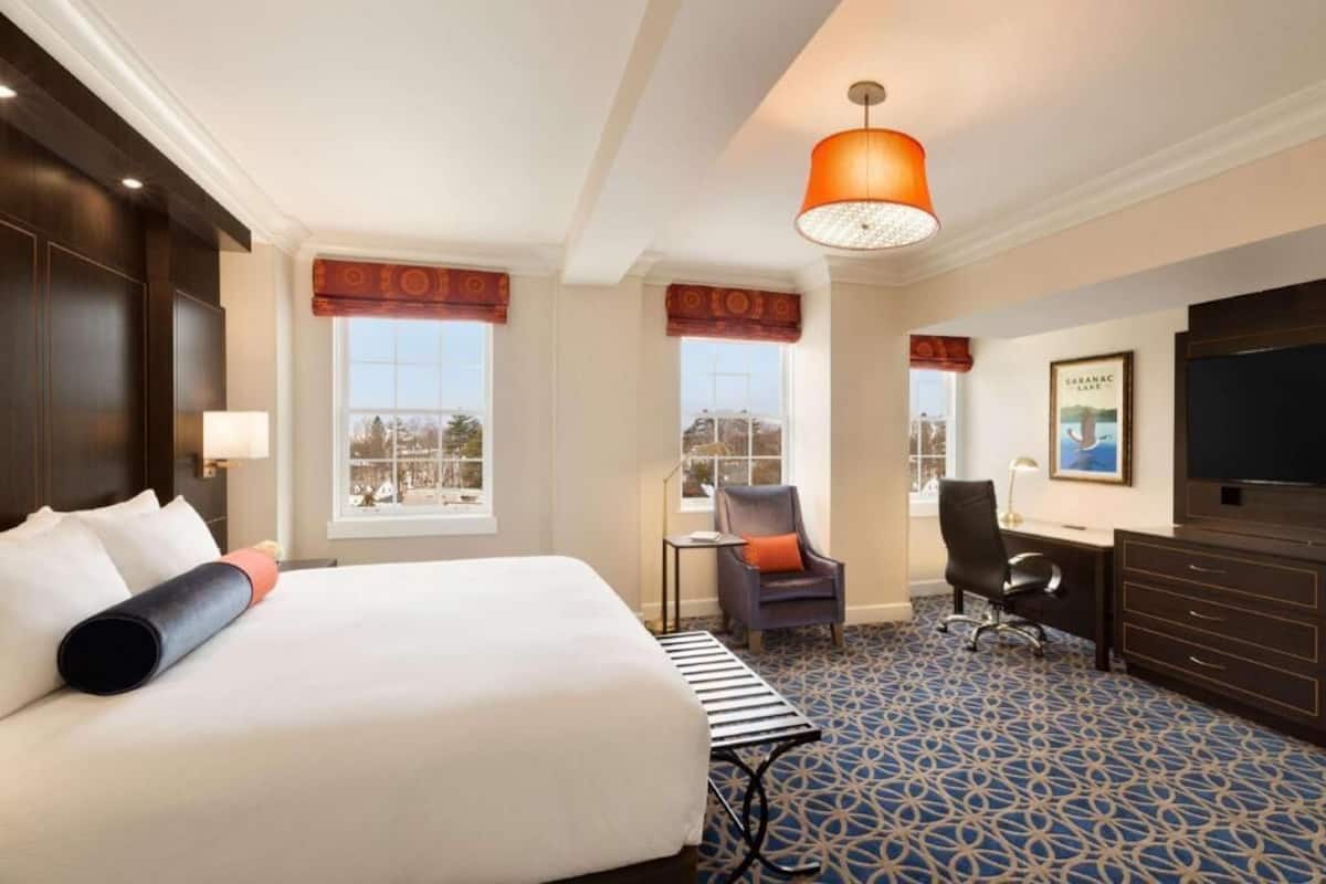 A hotel room with a large bed, a desk, a chair, a television, and a window with a view.