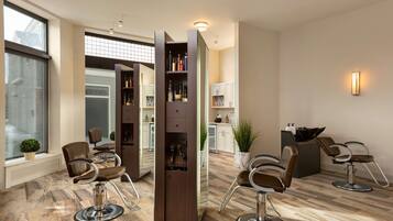 Ein moderner Friseursalon mit zwei Frisierstühlen, einem großen Spiegel und einem Bücherregal voller Produkte.