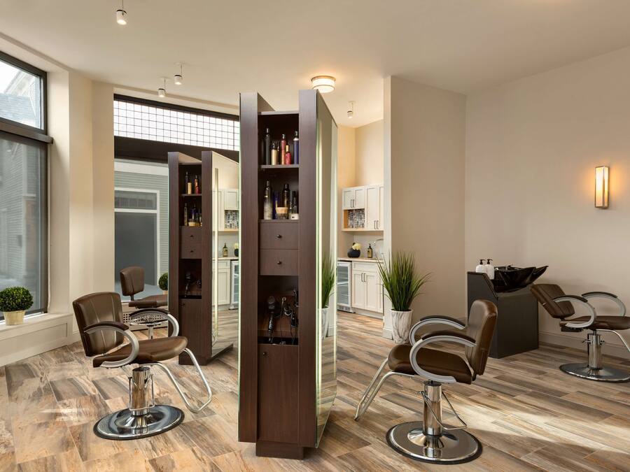 Ein moderner Friseursalon mit zwei Frisierstühlen, einem großen Spiegel und einem Bücherregal voller Produkte.