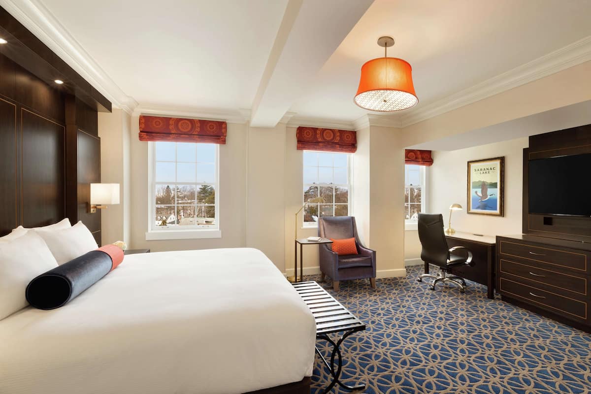 A hotel room with a large bed, a desk, a chair, and a television.
