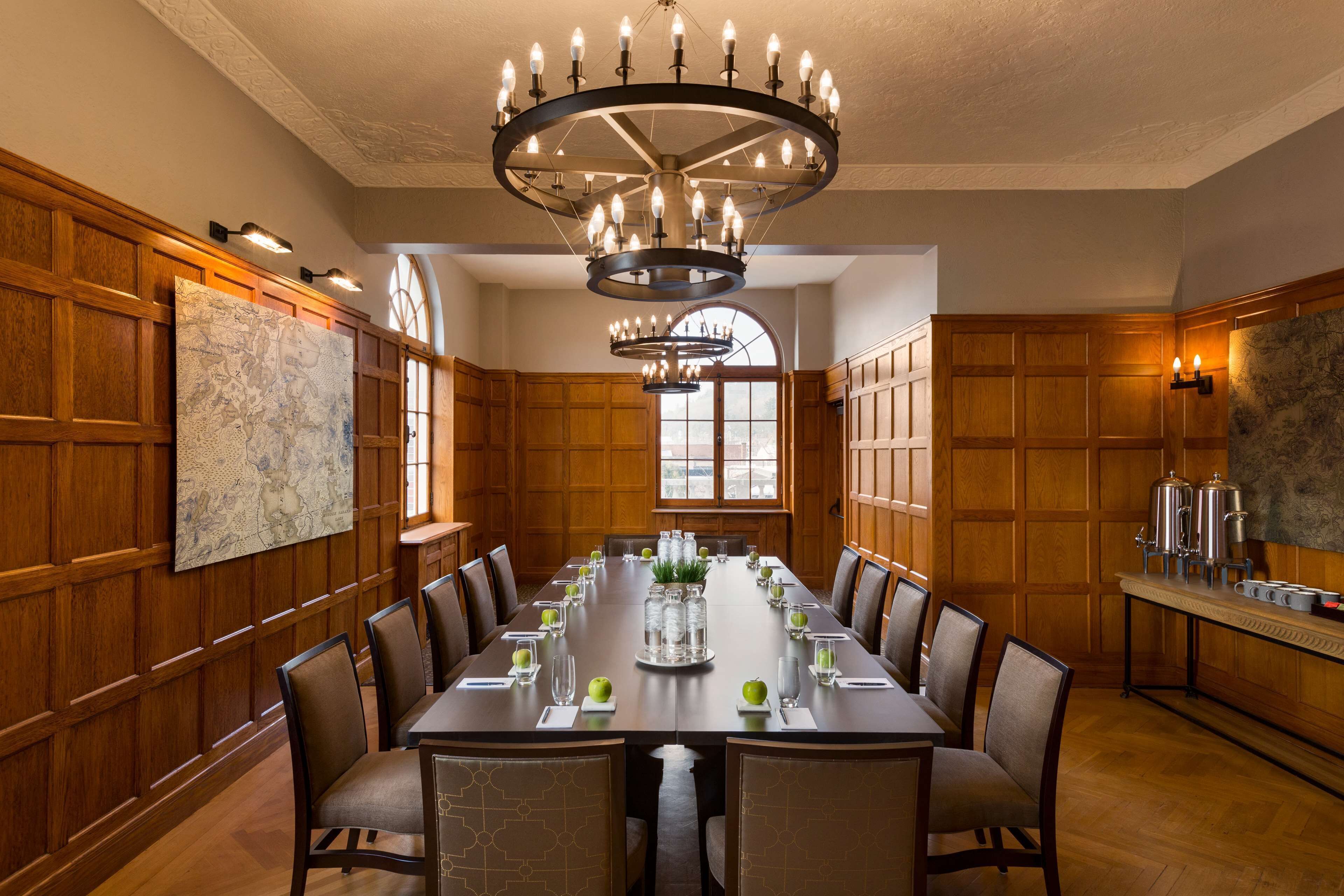 A conference room with a long table, chairs, a chandelier, wooden paneling, and a large window.