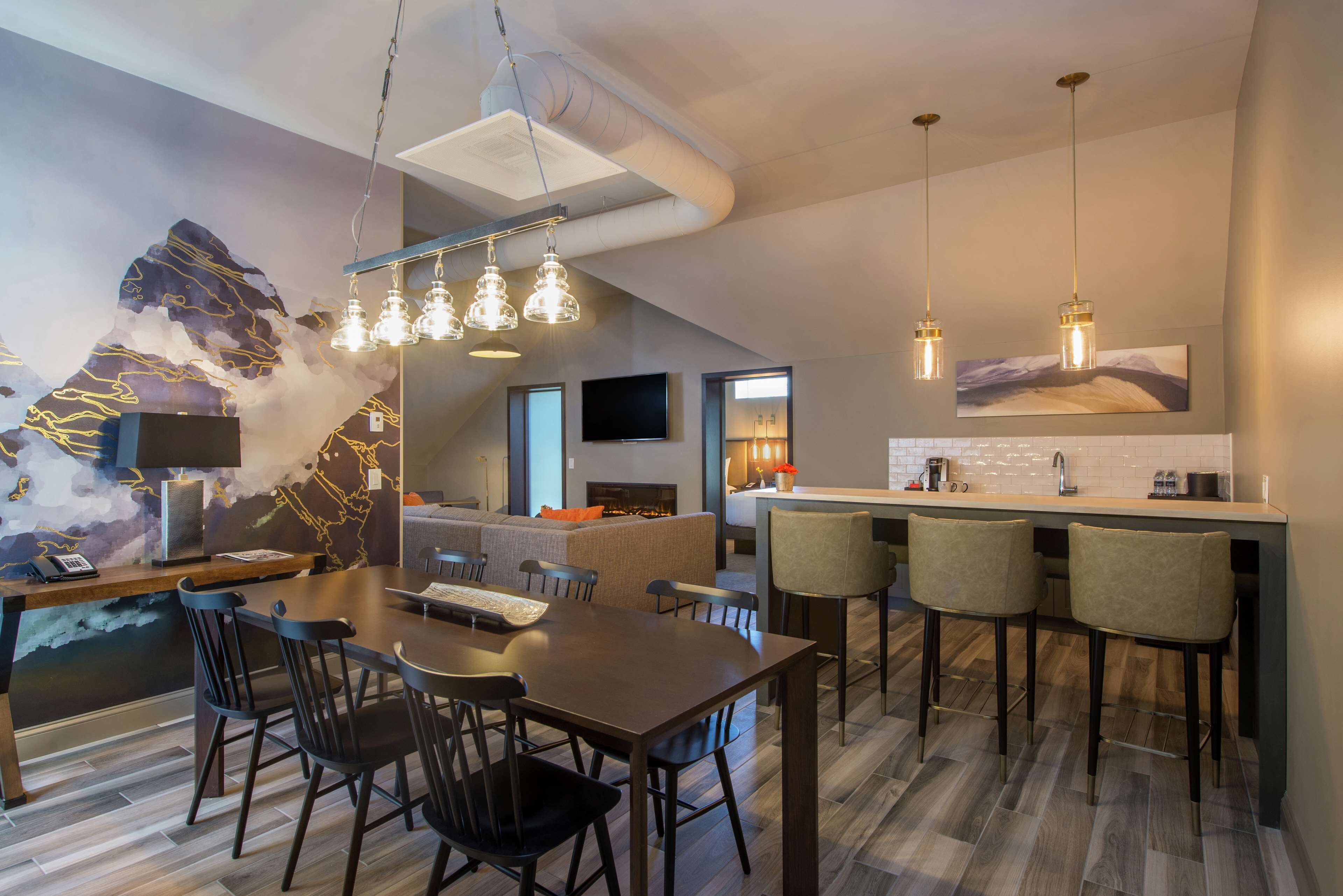 A modern kitchen with a bar area, a dining table with chairs, and a large abstract wall art piece.