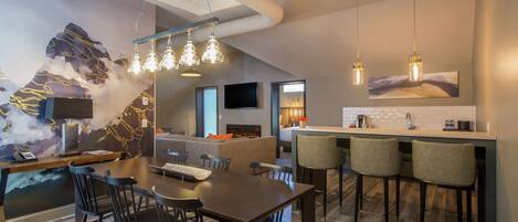 A modern kitchen with a bar area, a dining table with chairs, and a large abstract wall art piece.