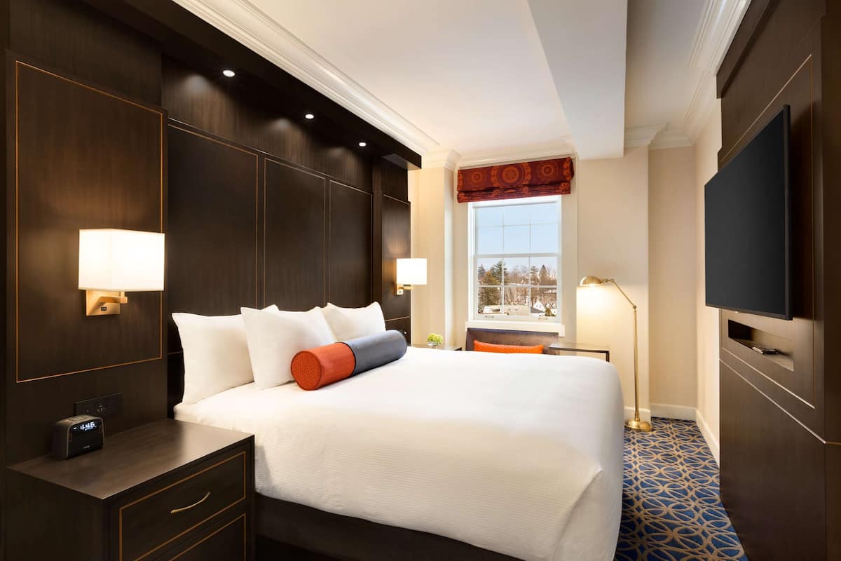 A hotel room with a large bed, bedside lamps, a flat-screen TV, and a window with a view.