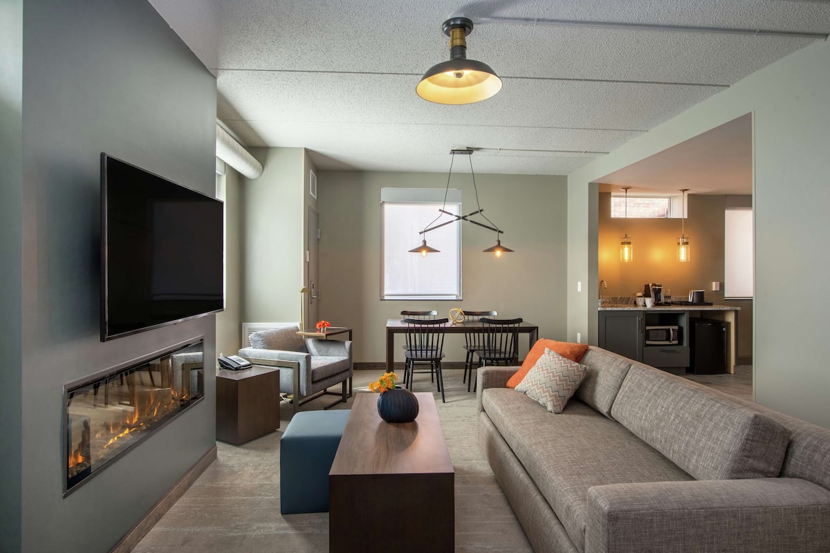 A modern living room with a flat-screen TV, a fireplace, a sofa, a coffee table, and a dining area with a table and chairs.