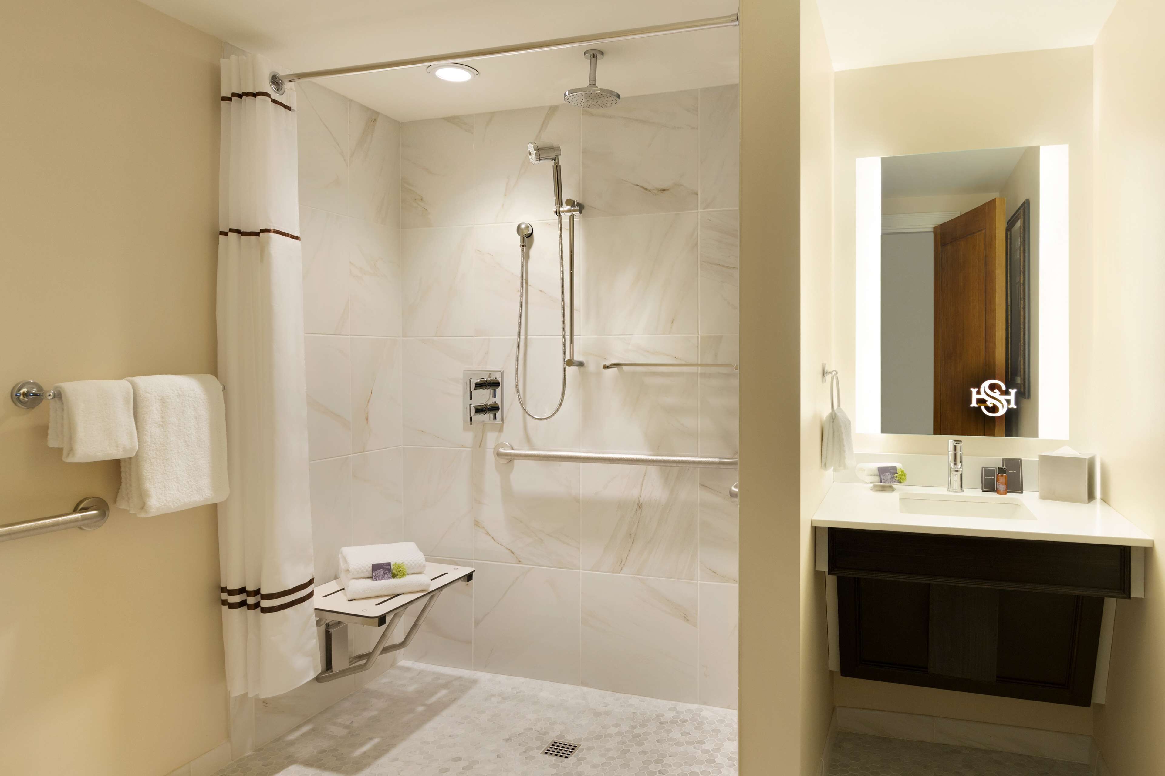 Une salle de bain moderne équipée d’une douche, d’un meuble-lavabo avec miroir et d’un porte-serviettes.