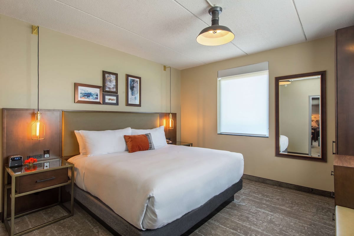A hotel room with a large bed, bedside tables, a nightstand, a mirror, and framed pictures on the wall.