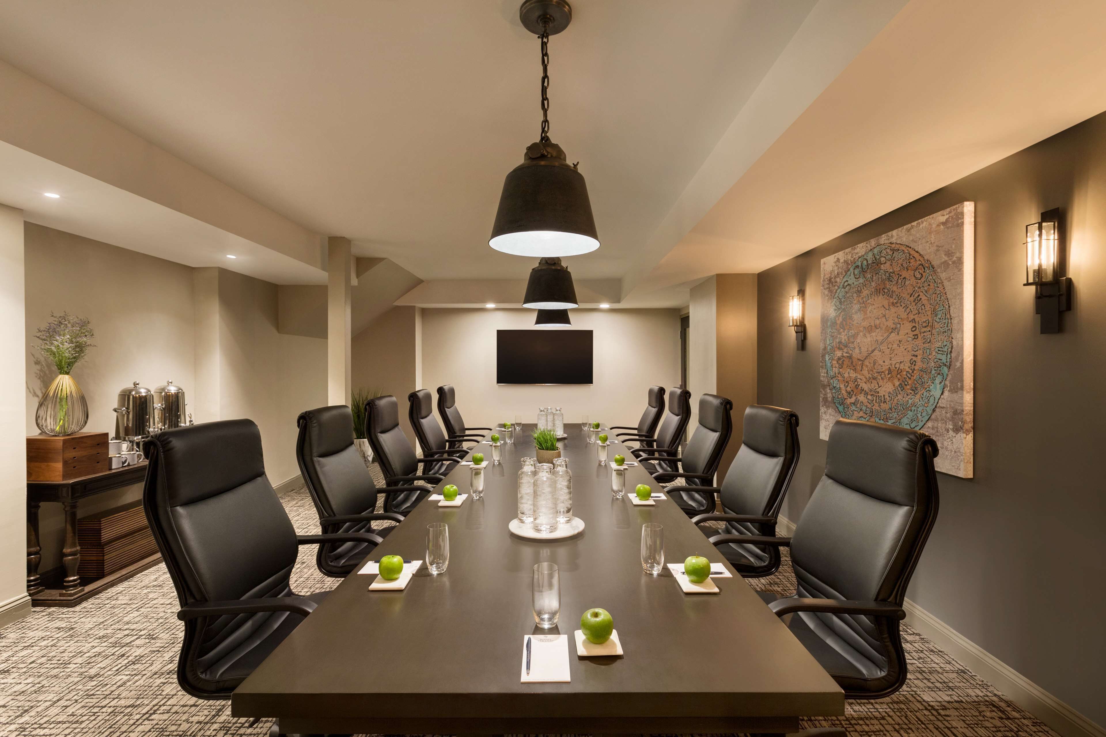 Une salle de conférence avec une longue table, des fauteuils en cuir noir, une plante au centre et une carte accrochée au mur.