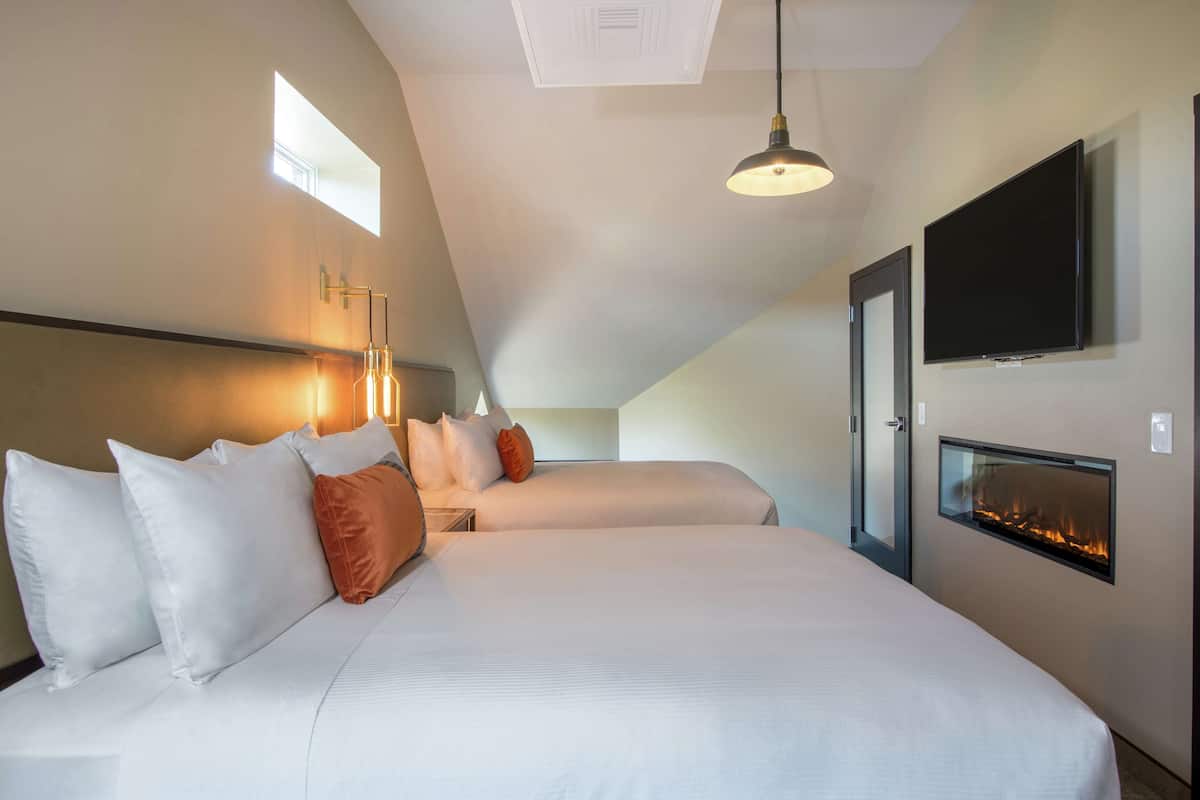 A modern hotel room with two beds, a fireplace, a TV, and a skylight.