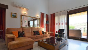 Una sala de estar con un sofá, una mesa de centro, una silla, un espejo y un balcón con una silla de mimbre.