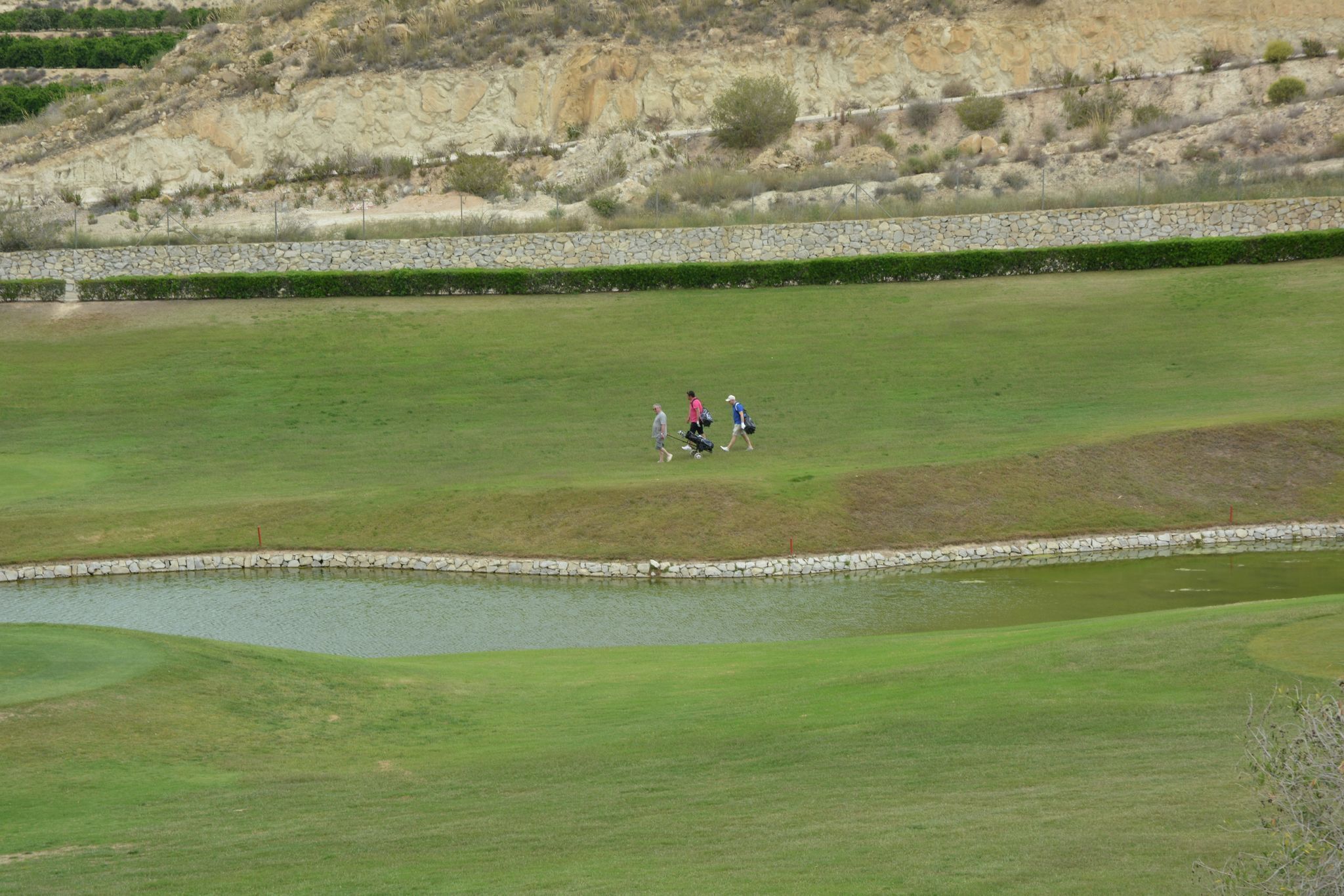 A golf course with a pond, stone walls, and a hilly background.