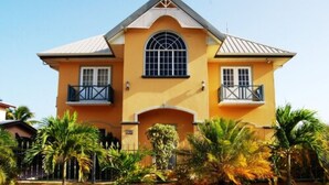 A two-story house with a yellow facade, a central arched window, and two balconies. - Casa Del Sol Tobago (Crown Point)