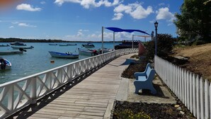 A wooden pier with a white railing, benches, and umbrellas providing shade. - Casa Del Sol Tobago (Crown Point)