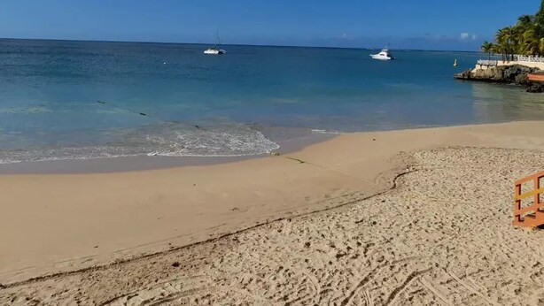 A beach with clear blue water, a sandy shore, and a few boats in the distance. - Casa Del Sol Tobago (Crown Point)