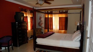 A four-poster bed with a wooden frame, a dresser with multiple drawers, a chair, and a ceiling fan. - Casa Del Sol Tobago (Crown Point)