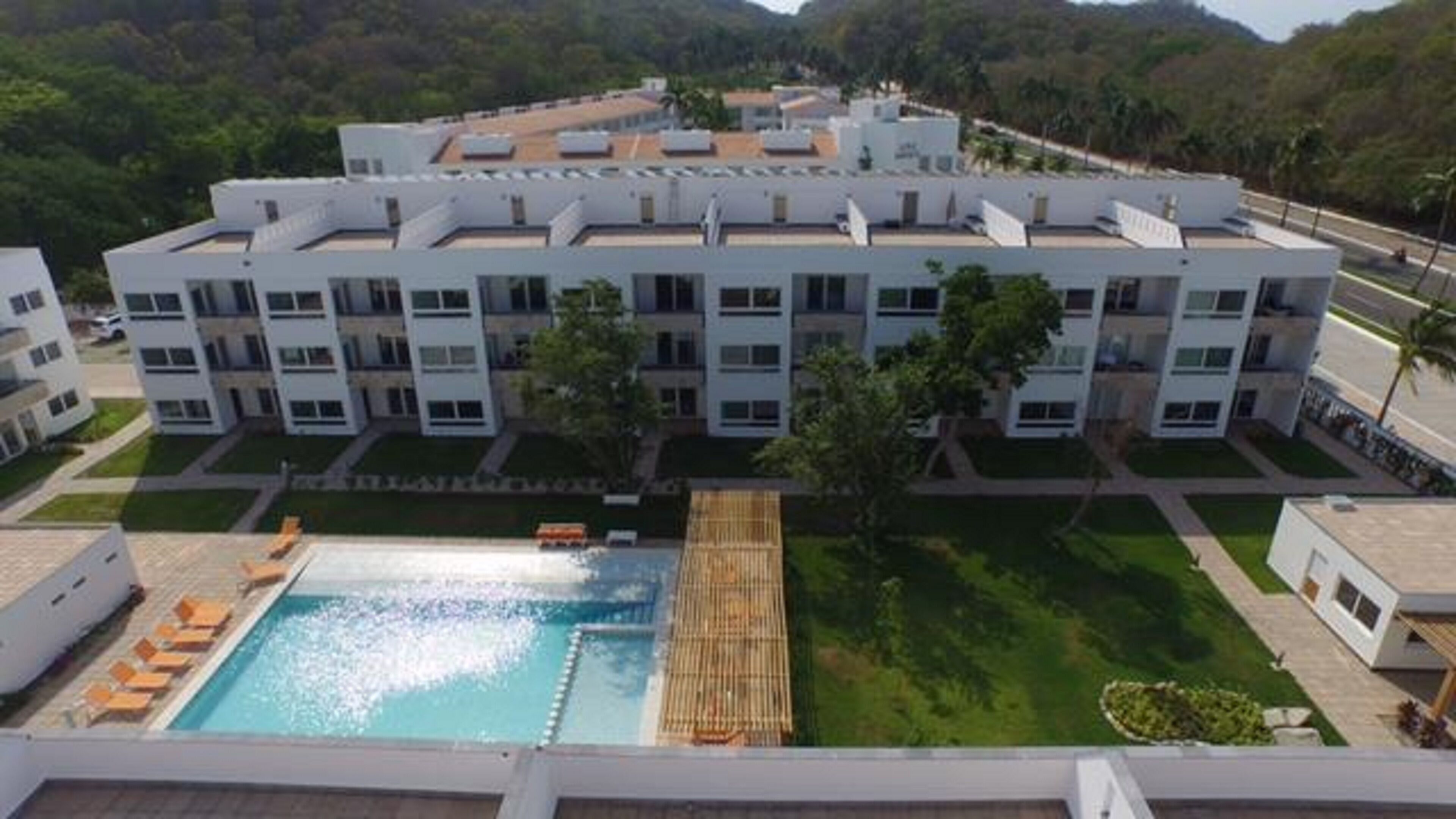 A modern multi-story hotel with a rooftop pool and a well-maintained lawn.