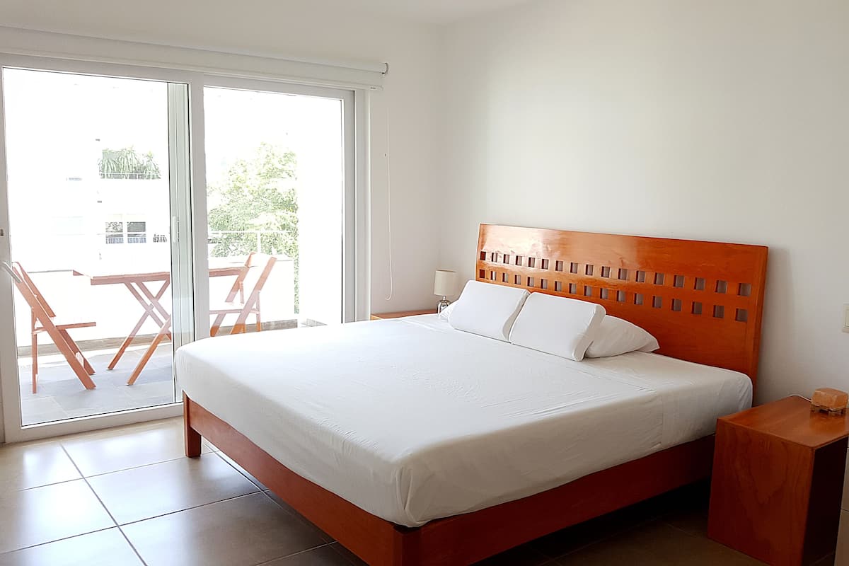 A bedroom with a wooden headboard, a bed with white bedding, a nightstand, a wooden cabinet, and a sliding glass door leading to an outdoor area with a table and chairs.