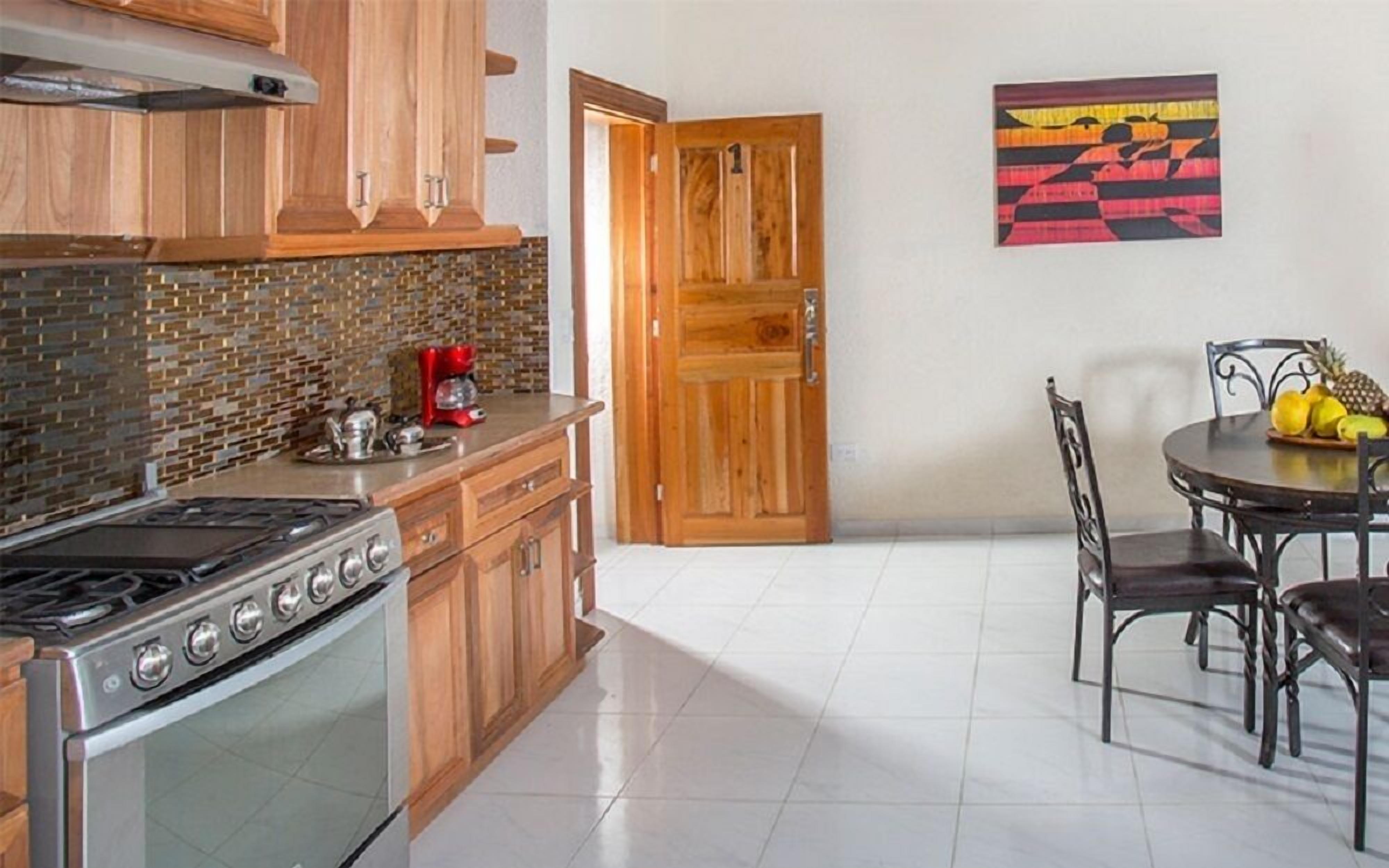 A kitchen with wooden cabinets, a stove, a coffee maker, and a dining area with a table and chairs.
