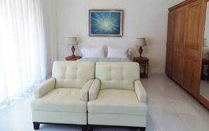 A room with a bed, a white sofa, two bedside tables with lamps, a wooden wardrobe, and a painting on the wall. - Residences Talou (Petionville)