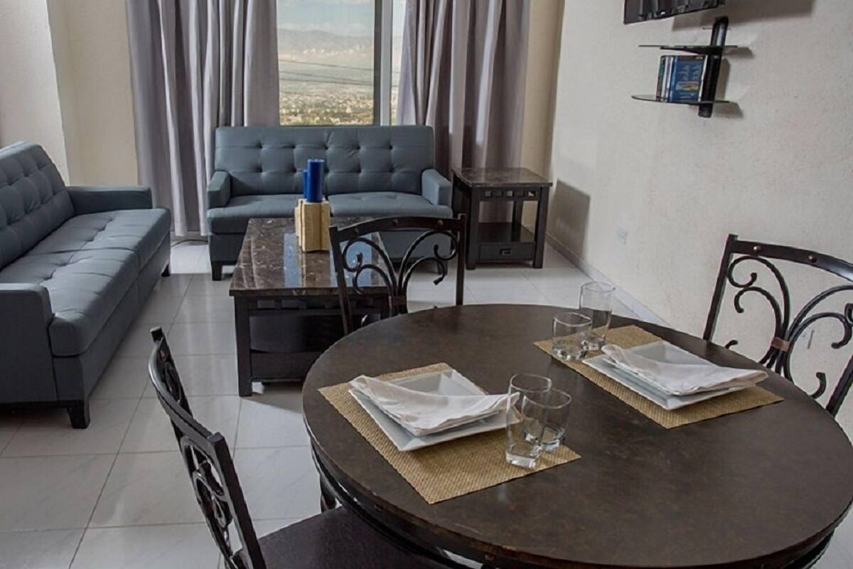 A modern living room with a grey sofa, a blue armchair, a wooden coffee table, and a dining table with chairs.