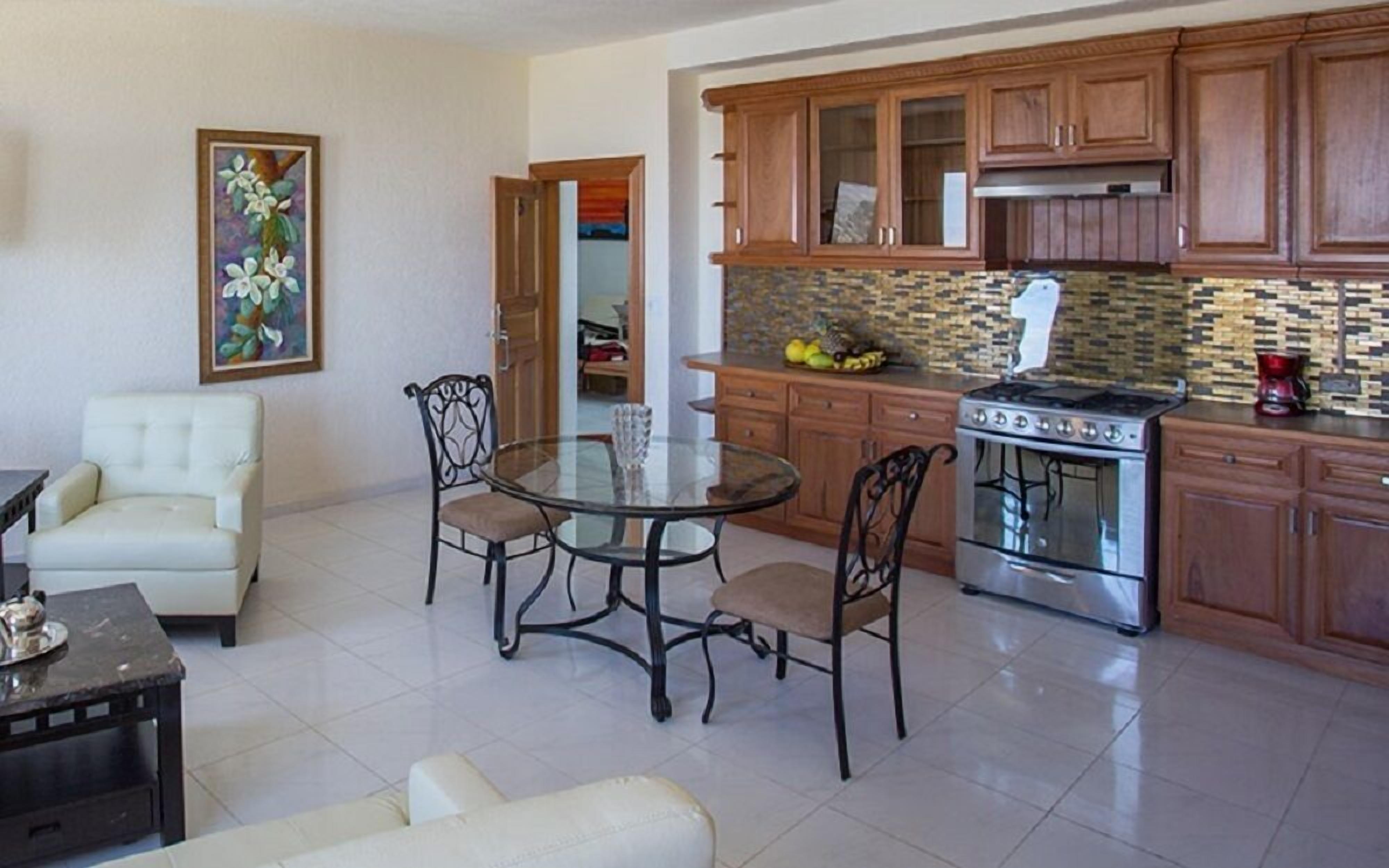 A modern kitchen with wooden cabinets, a gas stove, and a dining area with a glass table and chairs.