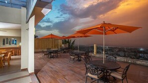 A rooftop terrace with wooden flooring, outdoor seating, and orange umbrellas. - Residences Talou (Petionville)