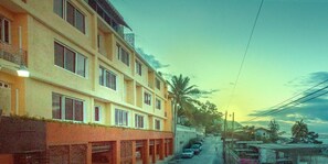 A multi-story building with a row of parked cars in front. - Residences Talou (Petionville)