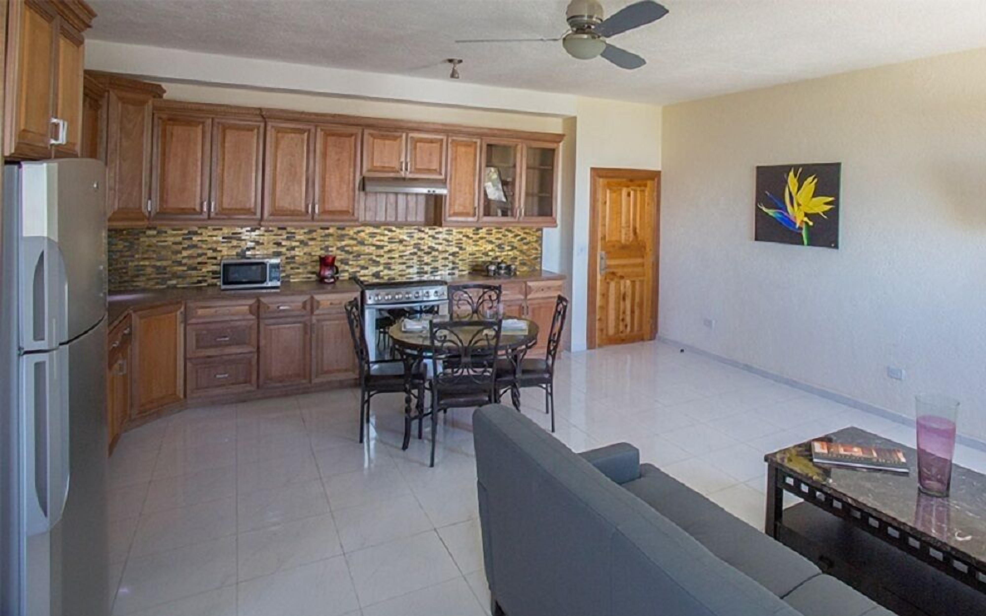 A kitchen with wooden cabinets, a microwave, and a stove. There is a dining table with chairs and a sofa in the living area.